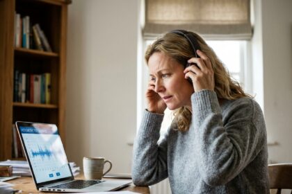 Femme d'une cinquantaine d'années effectuant un test auditif en ligne sur ordinateur portable avec un casque audio dans un bureau à domicile